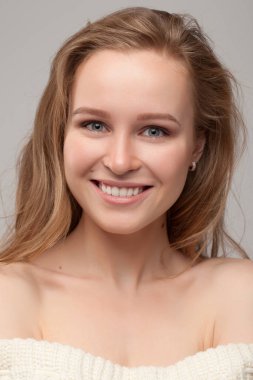 Güzel genç kız poz veriyor ve gülümsüyor. Beyaz kazaklı sarışın..