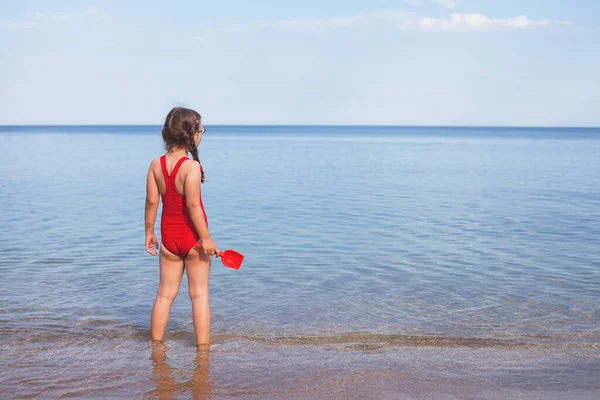 Kumsalda kırmızı mayolu genç ve güzel bir kız bulutlara bakıyor.