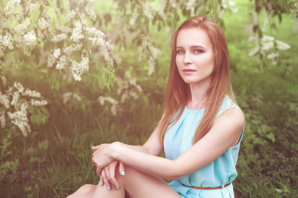 portrait of a young blonde girl in a blue dress. trees in flowers.