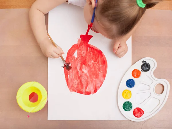 Yukarıdan bak. Çocuk bir fırça çizer ve beyaz kağıda resim yapar. kırmızı balon
