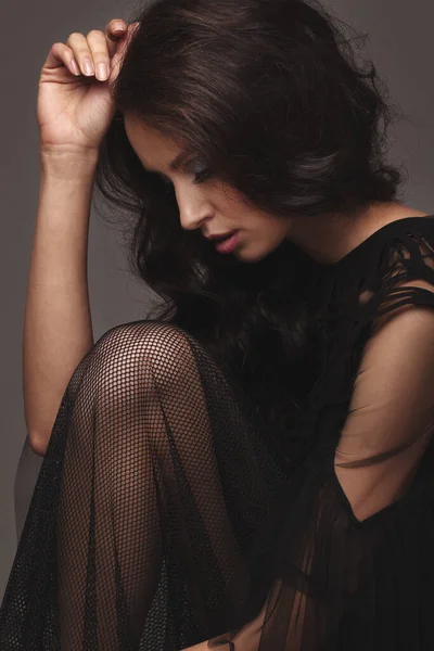 Siyah, seksi, şık elbiseli zayıf bir kız. Stüdyoda poz vermek. uzun siyah saçlar