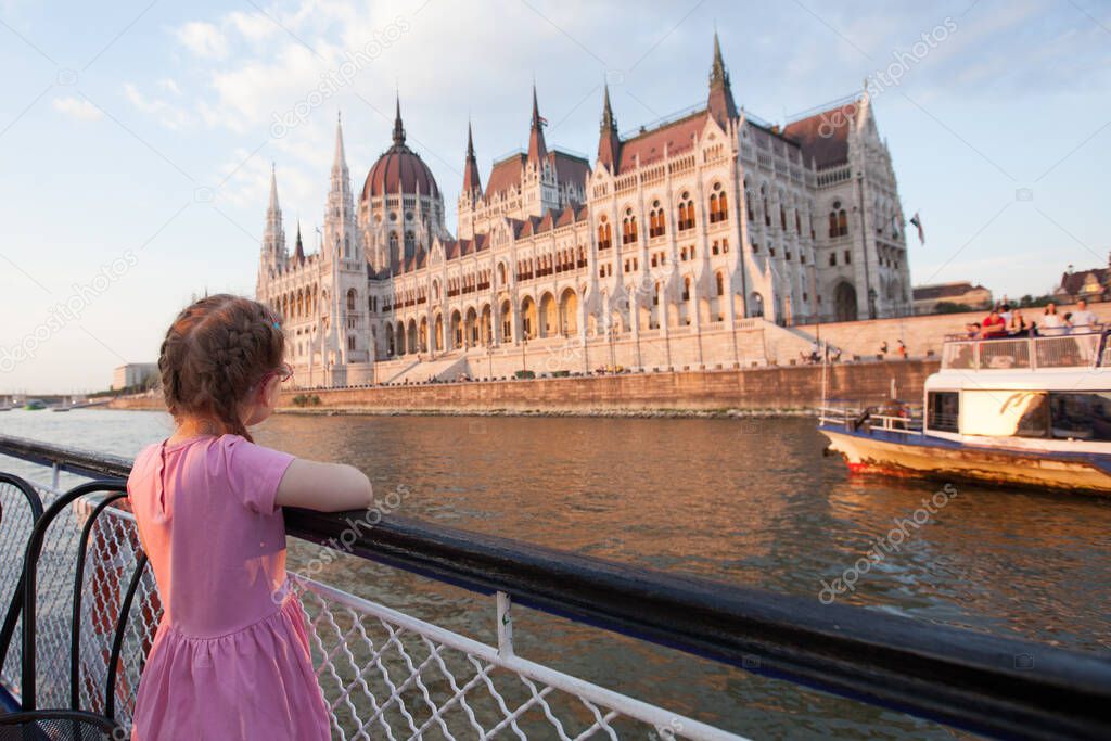 A little girl in red glasses sails on a ship on the Danube and looks at the parliament building in Budapest. young tourist