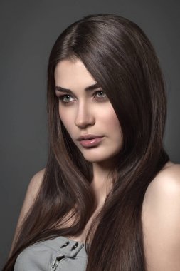 Güzel kız stüdyoda gri arka planda poz veriyor. Moda portresi. Makyaj malzemesi. Uzun saçlı..