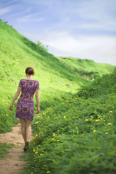 Kız tepeler arasında yeşil çimlerle kaplı bir patikaya çıkıyor. Yazın aydınlık güneşli günü.