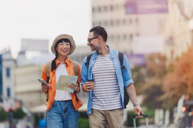 Happy tourists walking outdoors carrying map and luggage