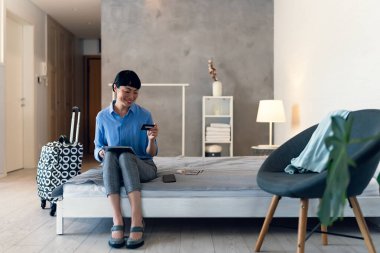 İş kadını modern yatak odasında tablet kullanarak yatakta oturuyor.