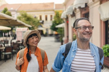 Smiling couple walking outdoors along sunny european street together