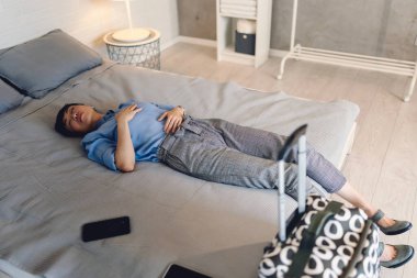 Yatakta bavul ve telefonla yatan kişi.