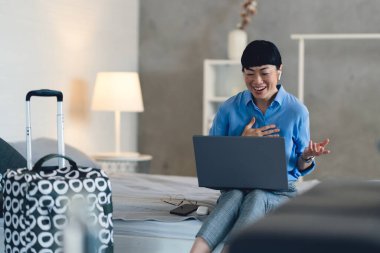 Smiling woman sitting on bed using laptop during video call
