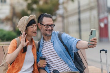 Smiling travellers sitting outdoors taking selfie together while traveling
