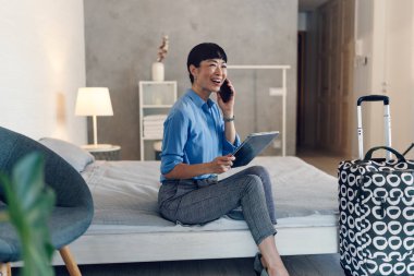 Smiling businesswoman sitting on bed talking using tablet device