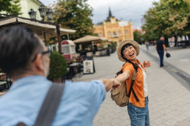 Smiling woman holding man's hand while walking outdoors happily