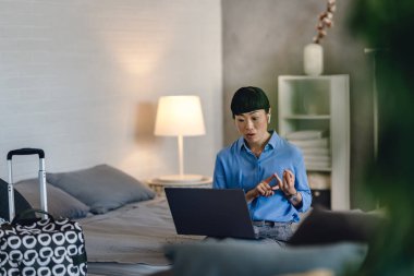 Woman sitting on bed using laptop during video conference call