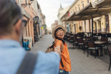 Smiling young woman holding hand walking through outdoor cafe street