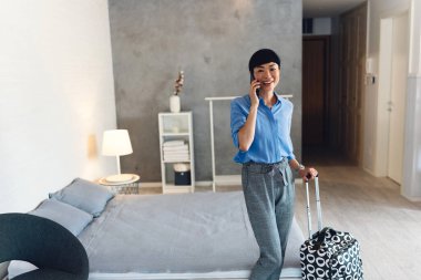 Woman standing near bed talking holding suitcase smiling indoors