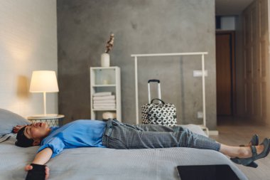 Tired woman resting on bed after arriving at hotel room