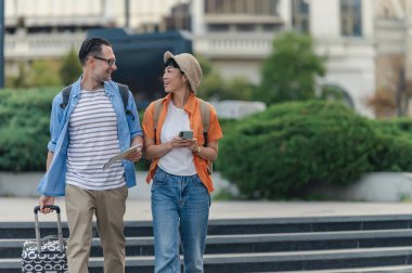 Smiling couple walking outdoors carrying suitcase and map together
