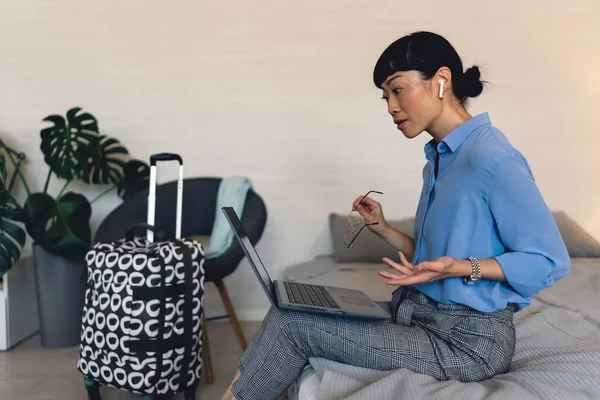 Yanında bavulu olan dizüstü bilgisayar kullanan bir kadın.