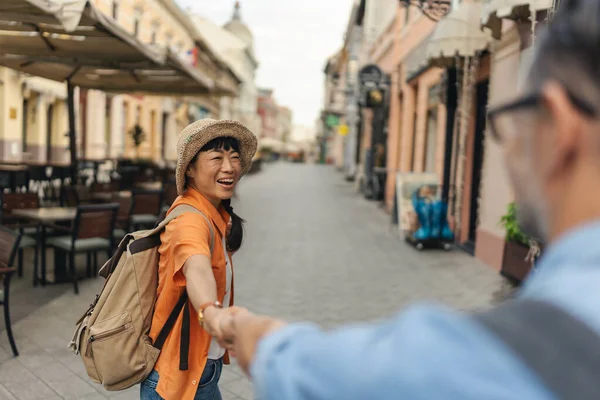 Smiling woman wearing hat holding hands walking along empty street