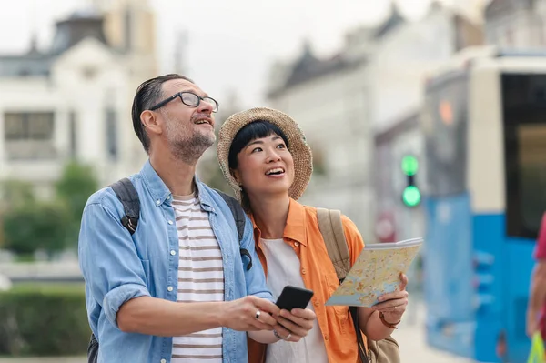 Smiling couple exploring city street holding map and smartphone outdoors