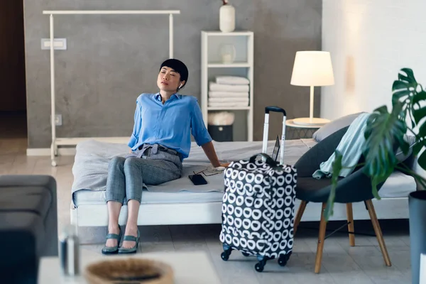 Woman relaxing on bed after arriving at modern hotel room