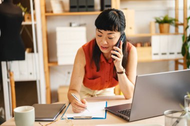 Woman talking on phone while writing notes at desk