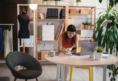 Woman working at modern desk using laptop and smartphone