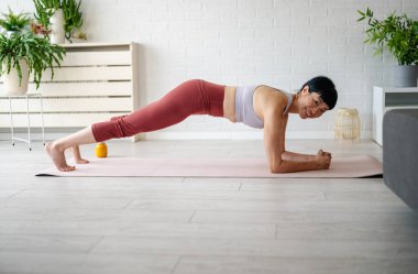 Woman practicing plank exercise indoors on yoga mat