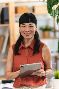 Smiling woman holding digital tablet standing near indoor plants