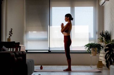 Woman practicing yoga indoors during morning sunlight near window