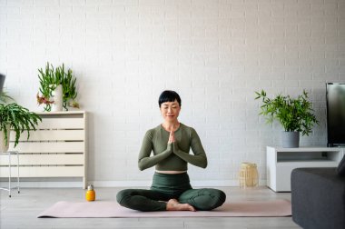 Woman practicing yoga meditation sitting cross-legged indoors near plants