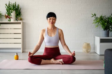 Woman practicing yoga meditation sitting cross-legged indoors peacefully smiling