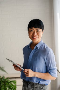 Smiling woman holding clipboard standing near bright window