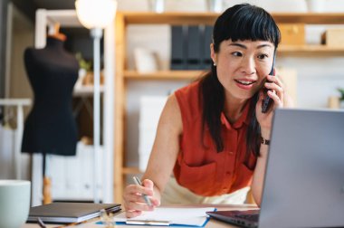 Smiling woman talking on phone while working at laptop desk