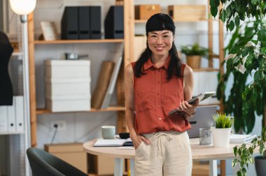 Smiling woman standing in modern office holding digital tablet