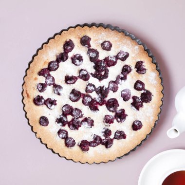 Çaydanlık ve bardak çay ile pastel pembe arka plan üzerinde tüm ev yapımı kiraz kek. Çok az. Düz kopya alanı ile yatıyordu.