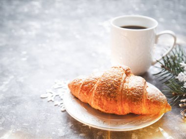 Bir fincan kahve ve taze kruvasan Noel ağacı garland tarafından aydınlatılmış bir tablo. Köknar dalı ve koni arka planda. Kış içecek konsepti. 