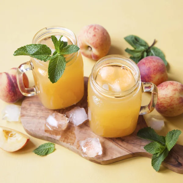 Cold summer peach drink with ice and mint in mason jars.
