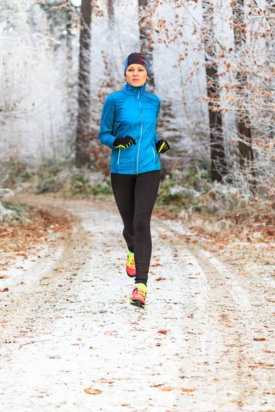 冬の森をジョギングする若い女性 — ストック写真