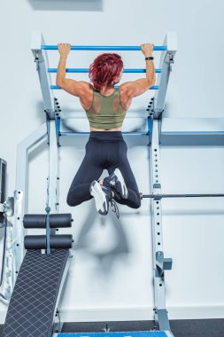 Spor salonunda ya da spor salonunda barfiks çubuğuyla çalışan bir kadın.