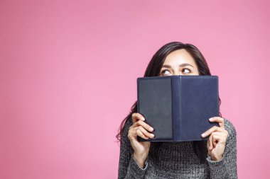 Ağzını kitap ile kapsayan bir genç kadının portresi kapatın ve seyir uzakta, pembe arka plan izole.