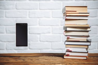 Modern smartphone ile boş perde ve masa üzerinde kitap yığını. Teknoloji vs geleneksel öğrenme eğitimi kavramı soyut