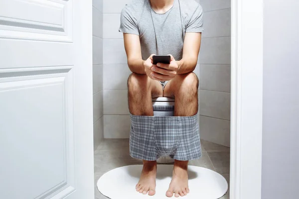 トイレに座ってのスマート フォンを持つ男 — ストック写真