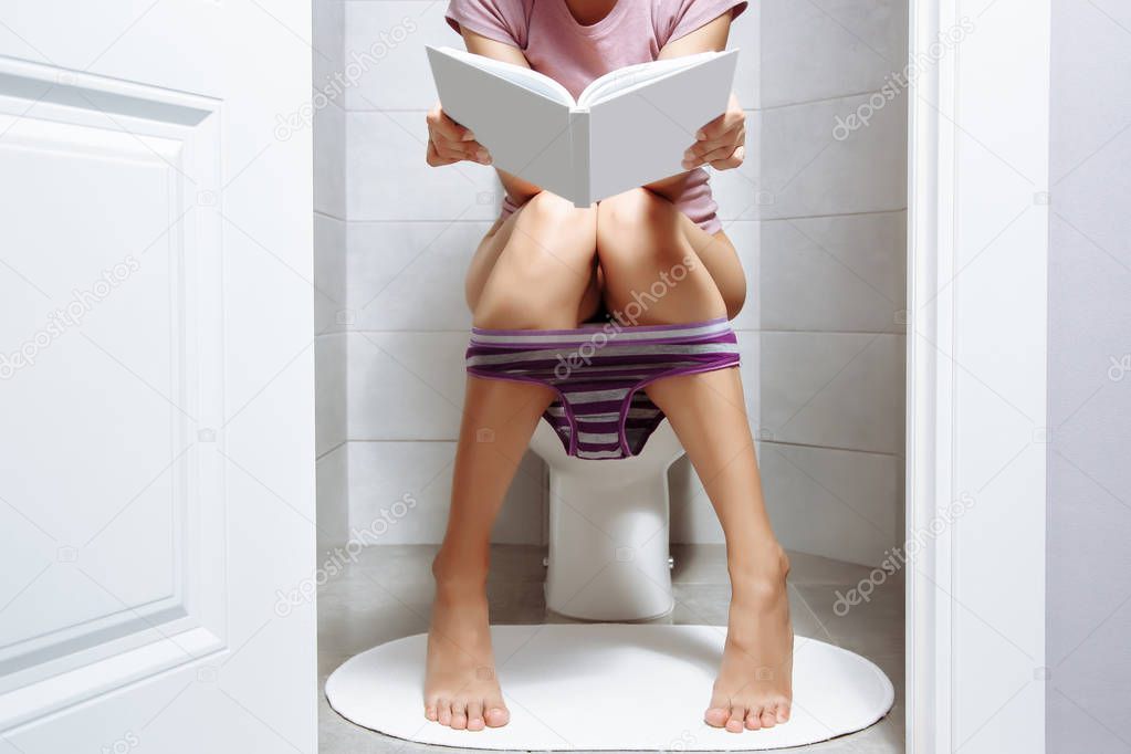Woman sitting on toilet bowl while reading book - health problem concept.