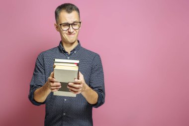 Pembe bir arka plan üzerinde kitapların bir yığınına ile şaşırmış adam.