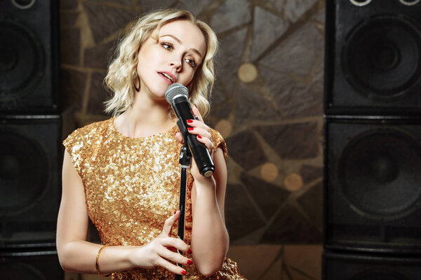 Портрет молодой блондинки с микрофоном на темном фоне
