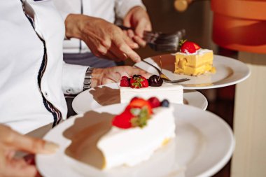 Kek parçaları ile tabak tutan garsonların ellerinin yakın çekim