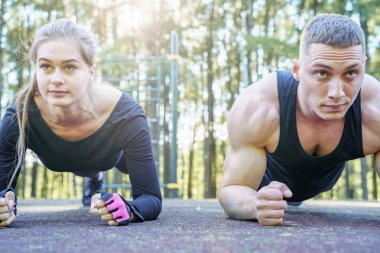 Açık havada plank egzersizi yapan genç sportif çiftin portresi.