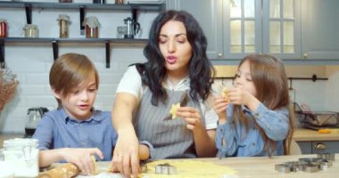 Mutlu aile, genç anne ve iki tatlı çocuk mutfakta kurabiye pişirirken birlikte eğleniyorlar..