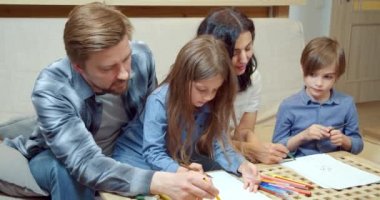 Mutlu yaratıcı aile, renkli kalemler ve keçeli kalemlerle çizim yapan iki sevimli çocuk. Evdeki kanepede birlikte oturuyorlar..